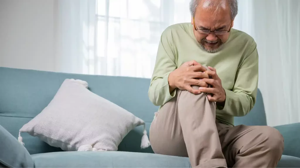 Older man sitting on a sofa holding his painful knee