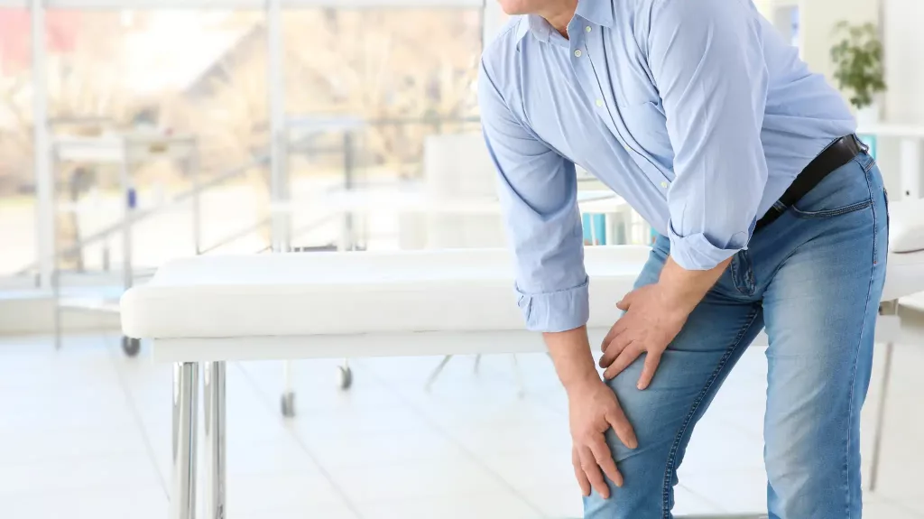 Man bending forward and holding his knee in a clinic
