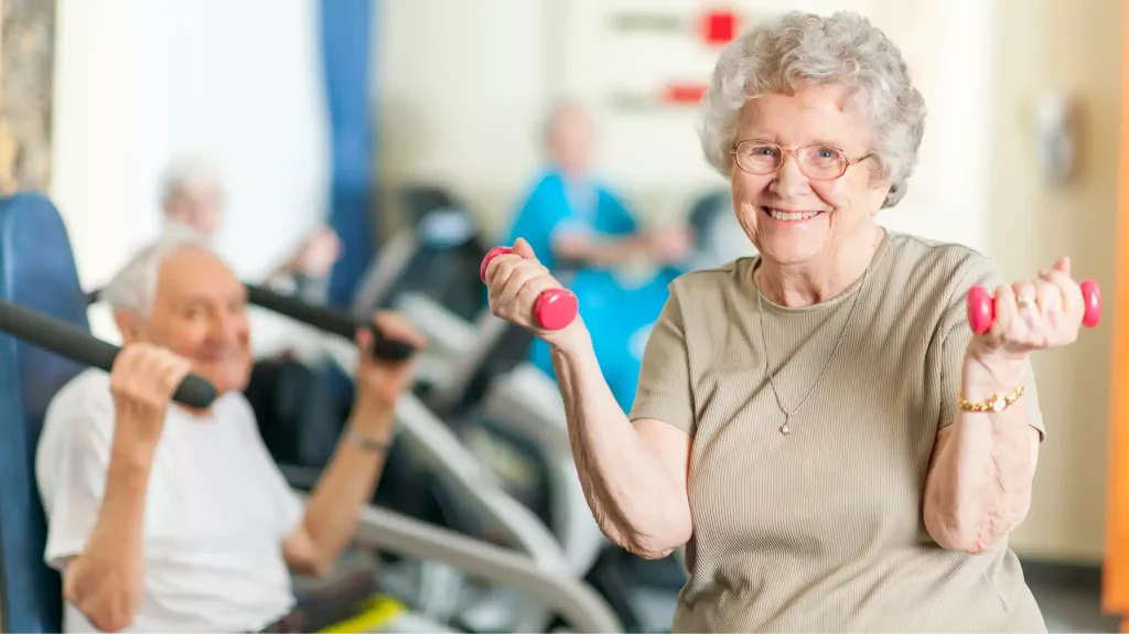 Older woman smiling while exercising with light hand weights in a gym